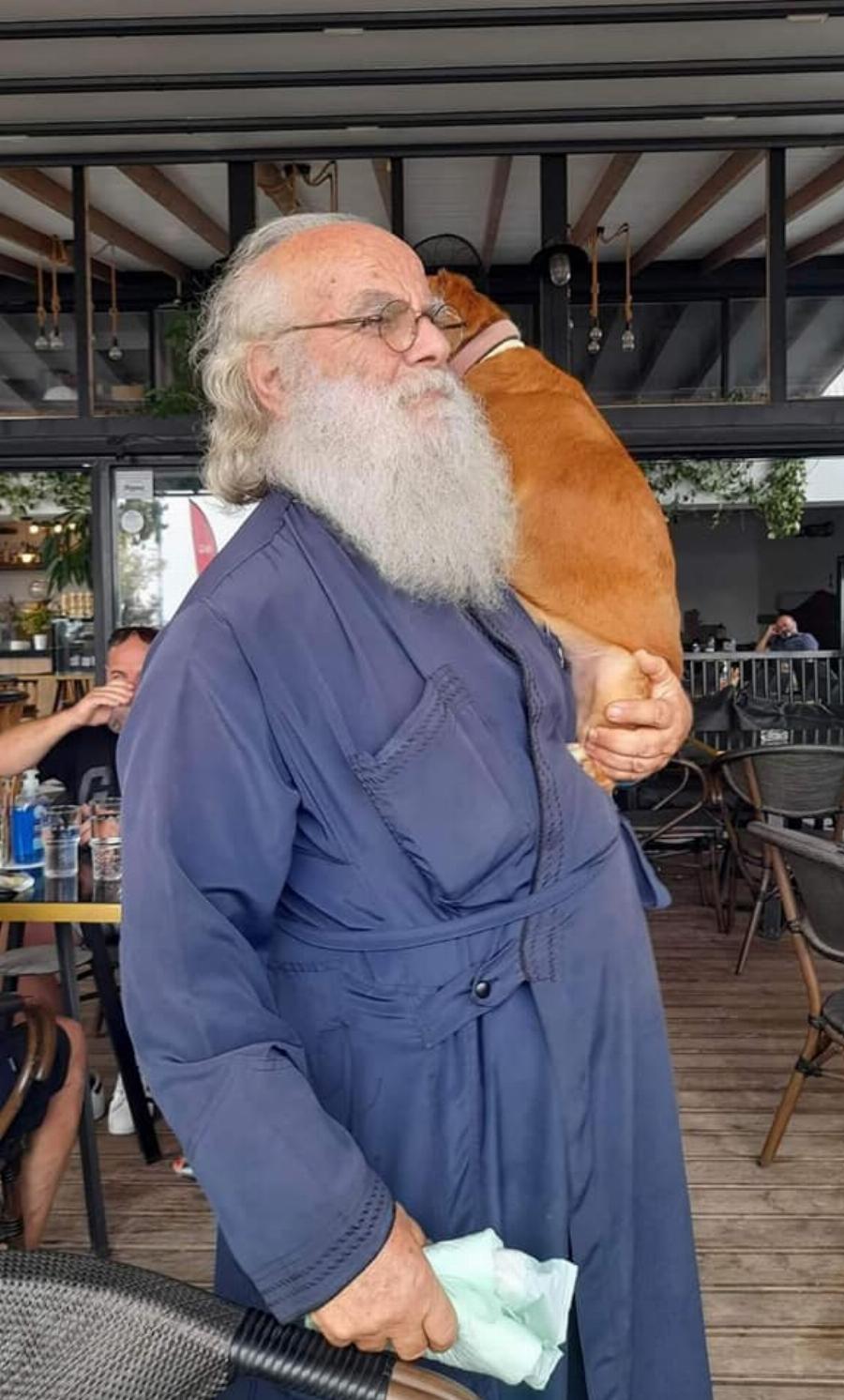 Ένας ιερέας διαφορετικός από τους άλλους στην Λέσβο: Κουβαλάει στα χέρια μια σκυλίτσα που έχει πρόβλημα με τη μέση της